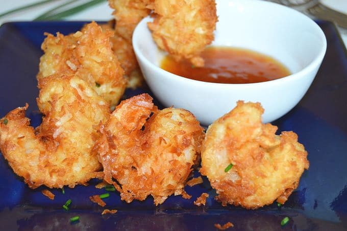 Crispy fried coconut shrimp on a blue plate with apricot sauce