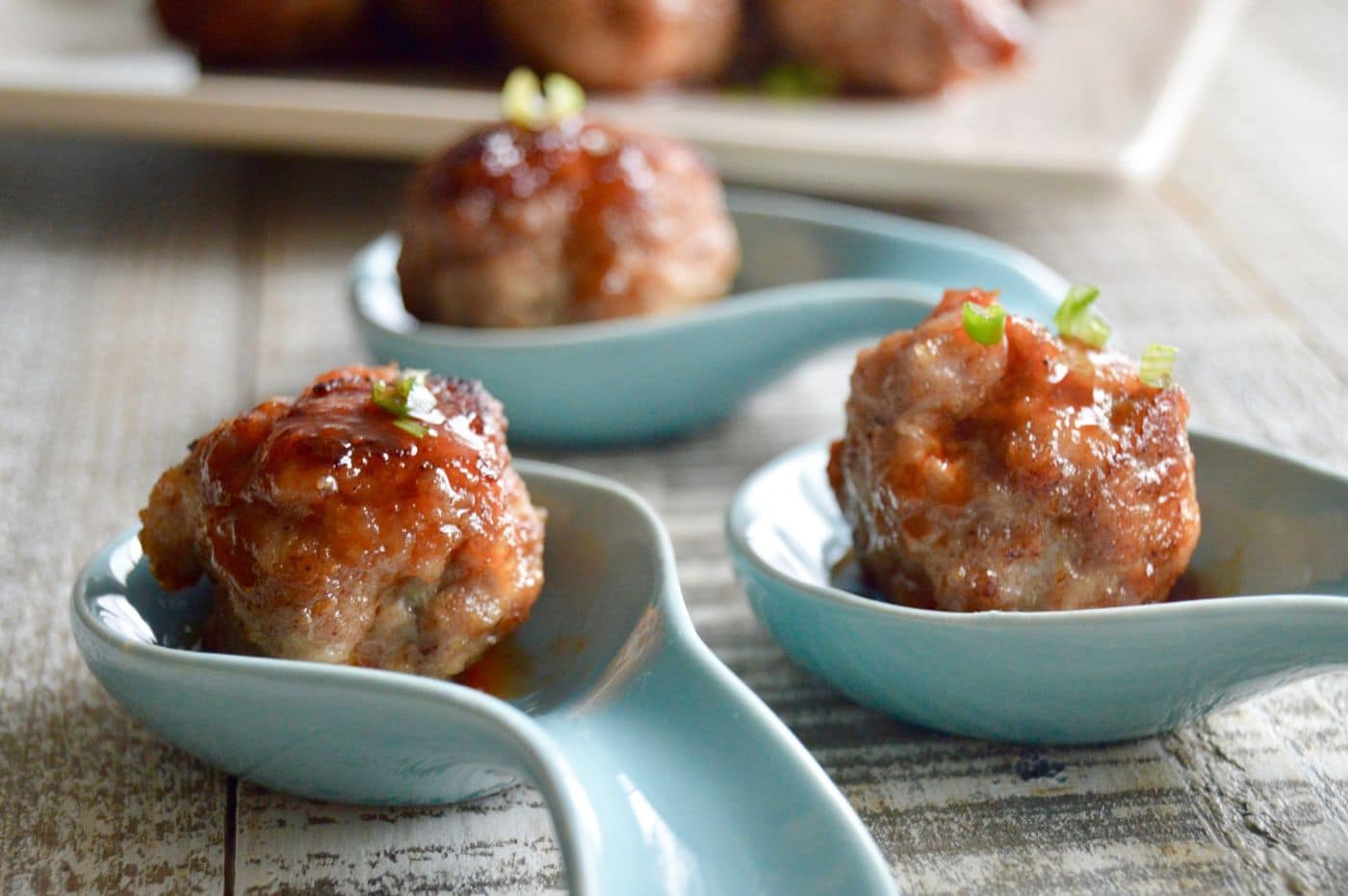Chinese Pork meatballs:Three meatballs served individually on spoons with a serving plate stacked high in the back!