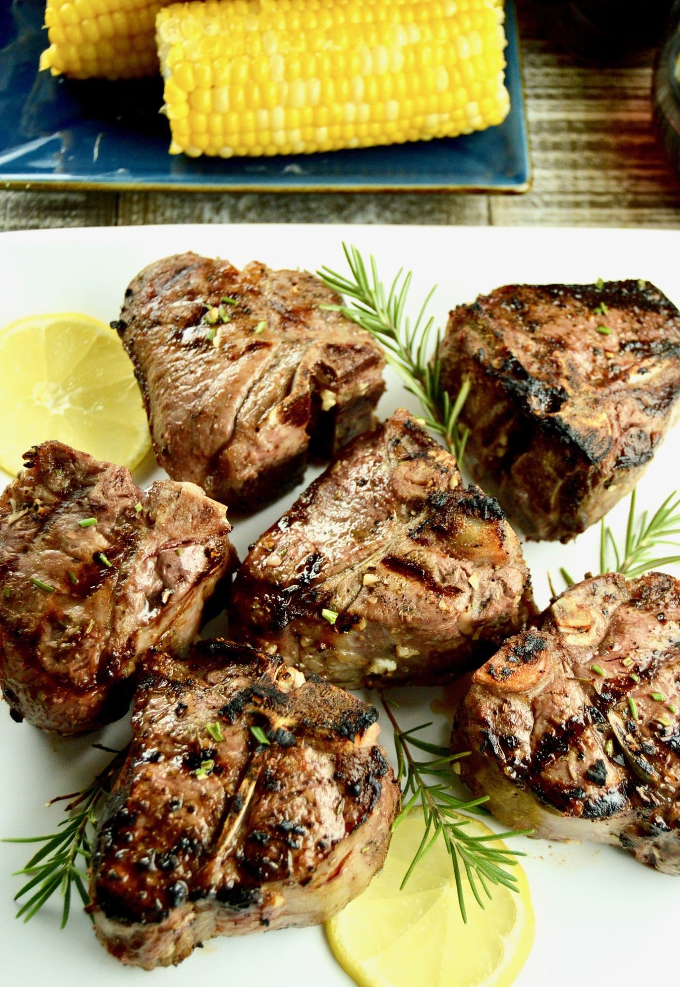 No Fail Grilled Lamb Chops a white serving platter with lemon slices and rosemary on a dining table