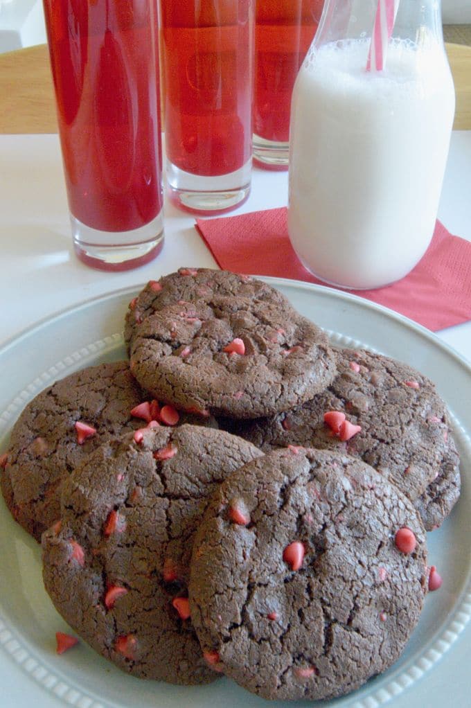 Chewy Chocolate Cookies.on a grey plate next to red vases and a large jar of milk with a red and white straw in it.