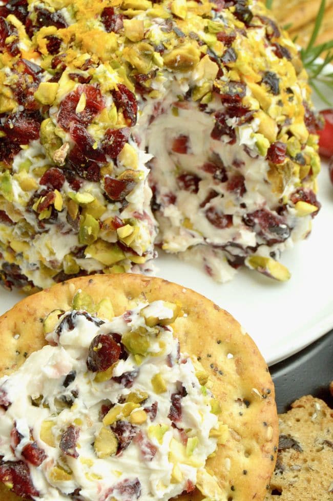 Cranberry Orange Cream Cheese dip ball on a white bowl, with a cracker with the cheese on top of it.