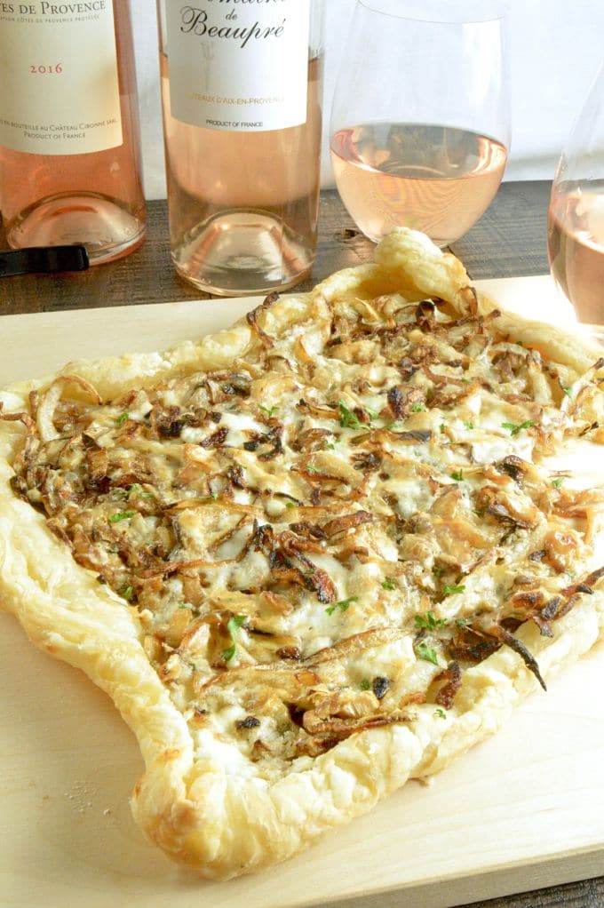 Caramelized Onion a top puff pastry for a French onion tart on a pizza board with wines of Provence in the background