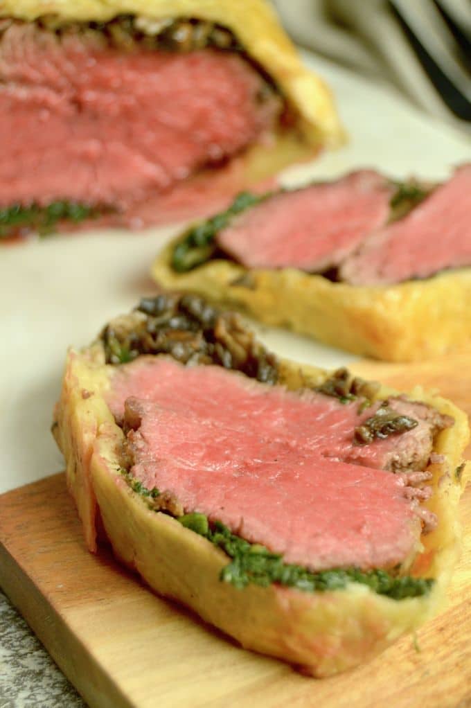 Beef Wellington Appetizers : shown with half finished puff pastry encased Wellington on a black plate with individual servings sliced off.