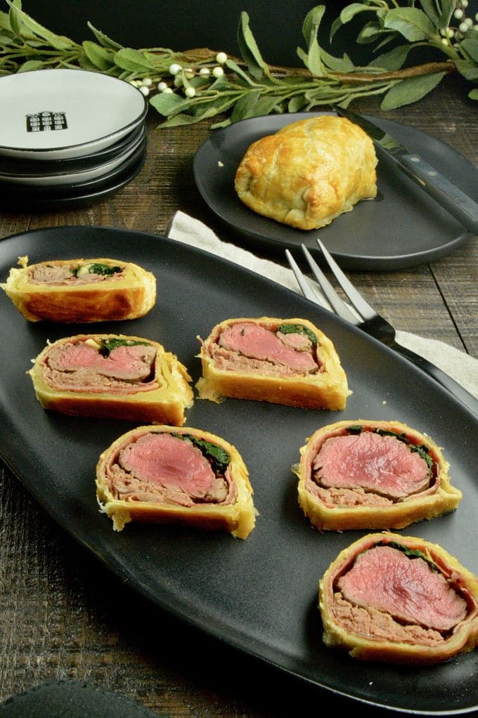 Beef Wellington Appetizers:  All cut on a black serving plate with the half of the log uncut in the background