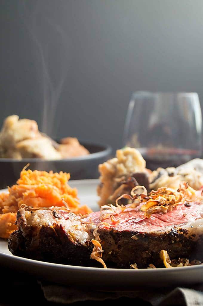 Dinner tabletop setting of Horseradish crusted Prime Rib Roast with a class of wine and a steaming bowl of fresh Mushroom Bread Pudding