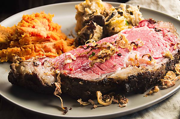 Horseradish Mustard Crusted Prime Rib Roast is tender, juicy and all the deliciousness you pay a fortune for at a fancy restaurant. Here a closeup of the mouthwatering slice on a tan plate with crunch horseradish tendrils galling off the meat.