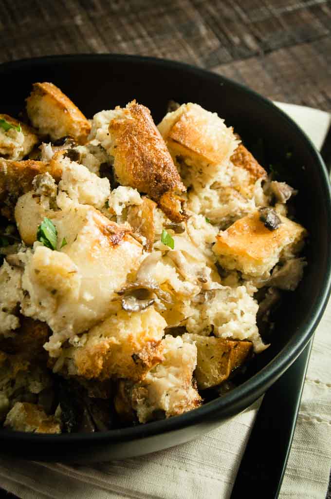 Black Bowl filled with Easy Savory Bread Pudding with exotic mushrooms on top of a natural colored napkin.