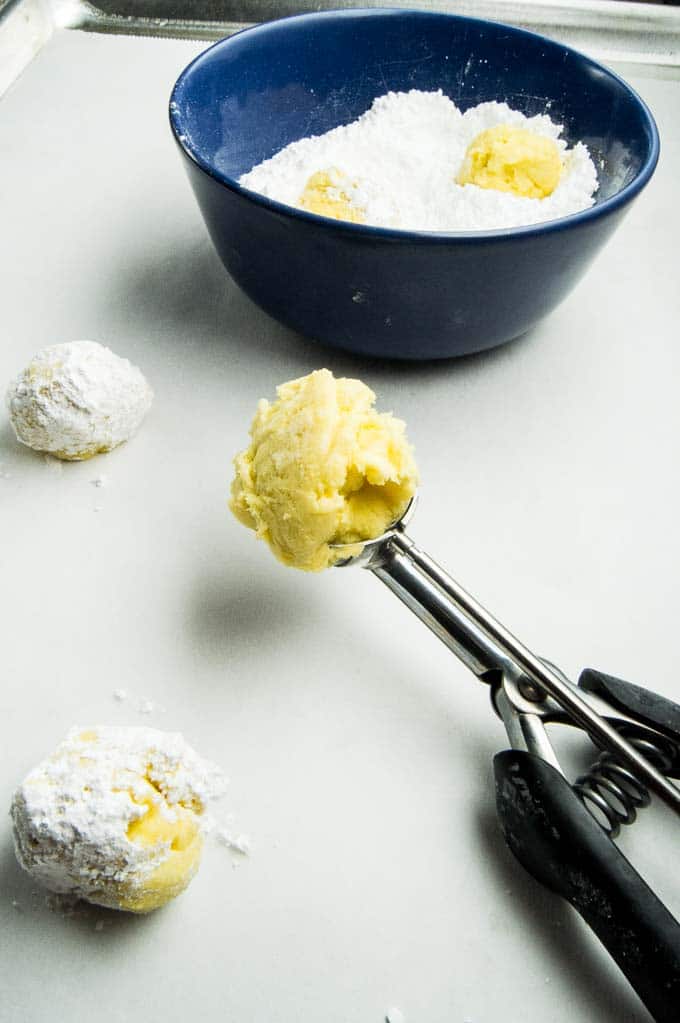 Process shot of Gooey Lemon Butter cookies being made in a scoop and dipped into powdered sugar.