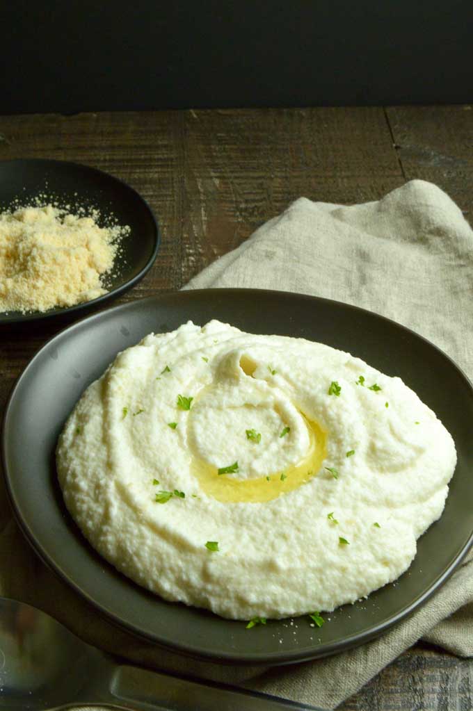 Creamy Cauliflower Puree in a black bowl drizzled with olive oil.