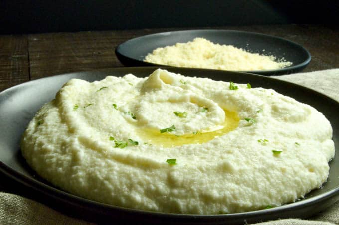 Creamy Cauliflower Mashed Puree with parmesan cheese for topping in a bowl behind.