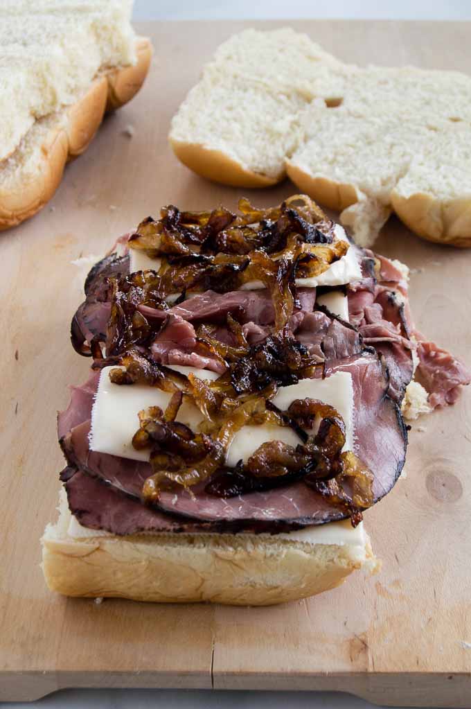 Stacking grilled onions and cheese onto roast beef on the Beef Sliders for super bowl party food