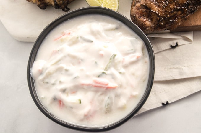 Tzatziki Sauce in a black bowl next to chicken in the background