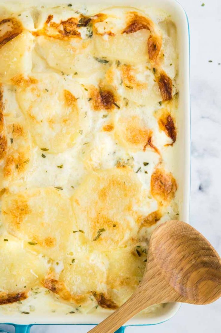 Pan Full of Scalloped Potatoes with a wooden spoon