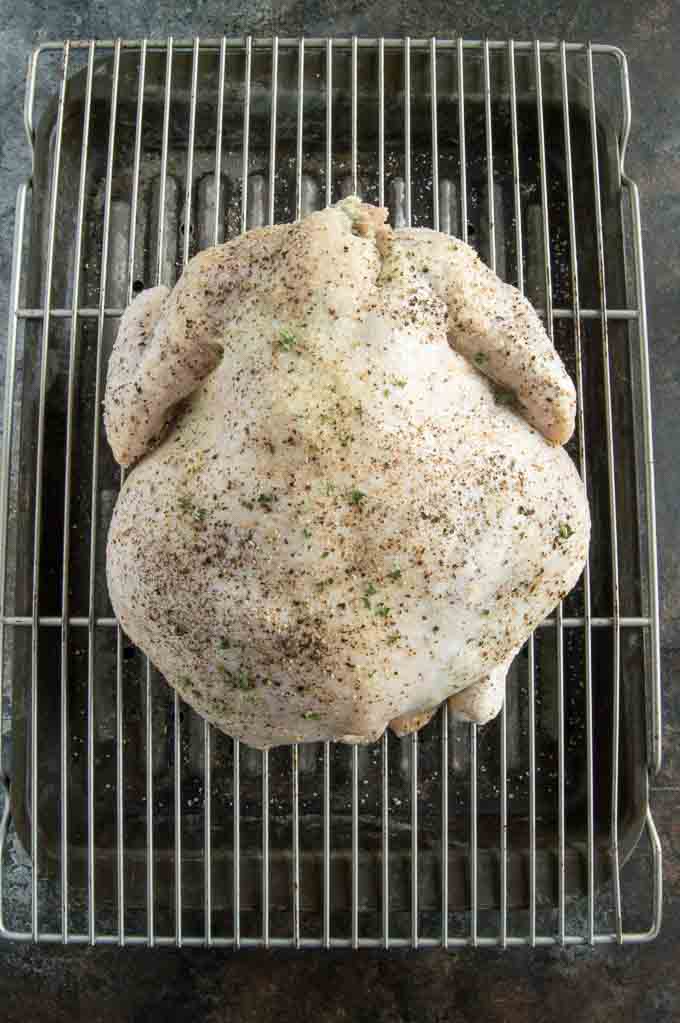 Fully salted and peppered roast chicken on rack to go into the oven