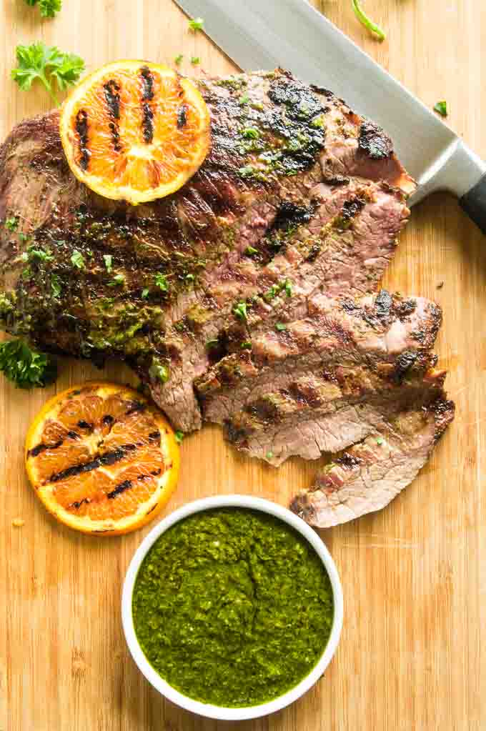 Flank Steak with chimichurri sauce sliced on a cutting board. 