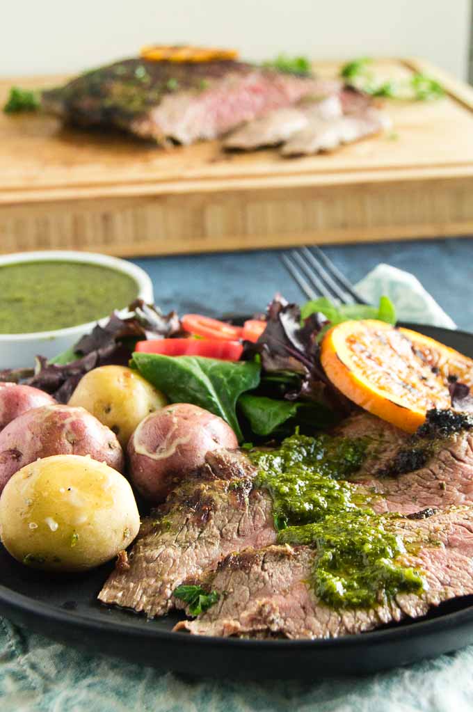 Sliced flank steak topped with a spoonful of fresh chimichurri sauce.