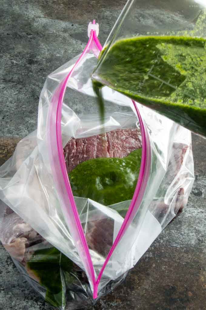 Pouring chimichurri sauce over the skirt steak to marinate.