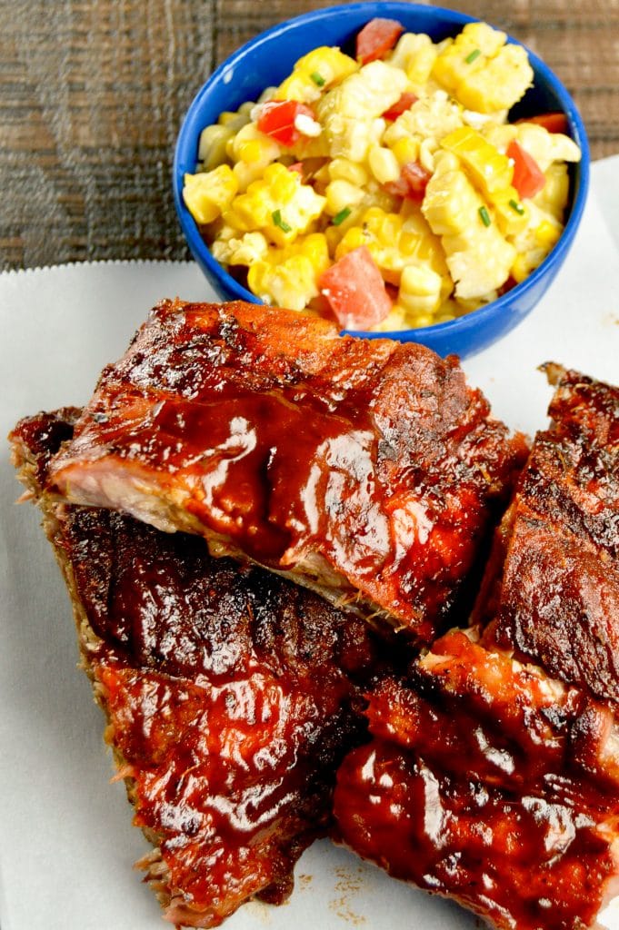 Ribs stacked on a white paper with corn in back