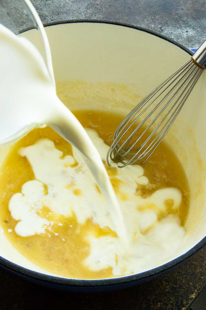 milk being poured into the flour roux to create a sauce