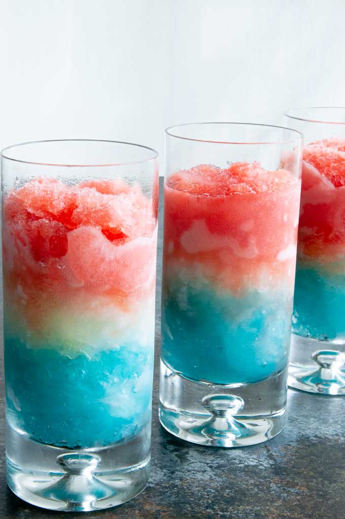 Three red white and blue layered cocktails lined in a row in tall glasses.