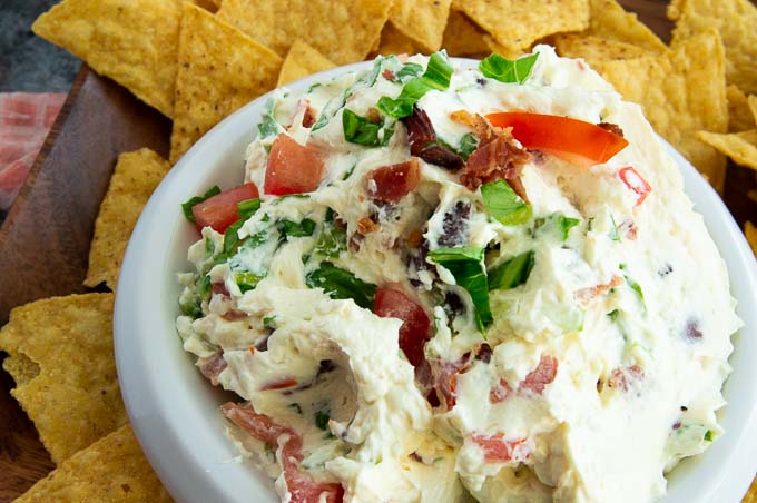 Fresh cream cheese dip with bacon lettuce and tomatoes inside and on top for serving.
