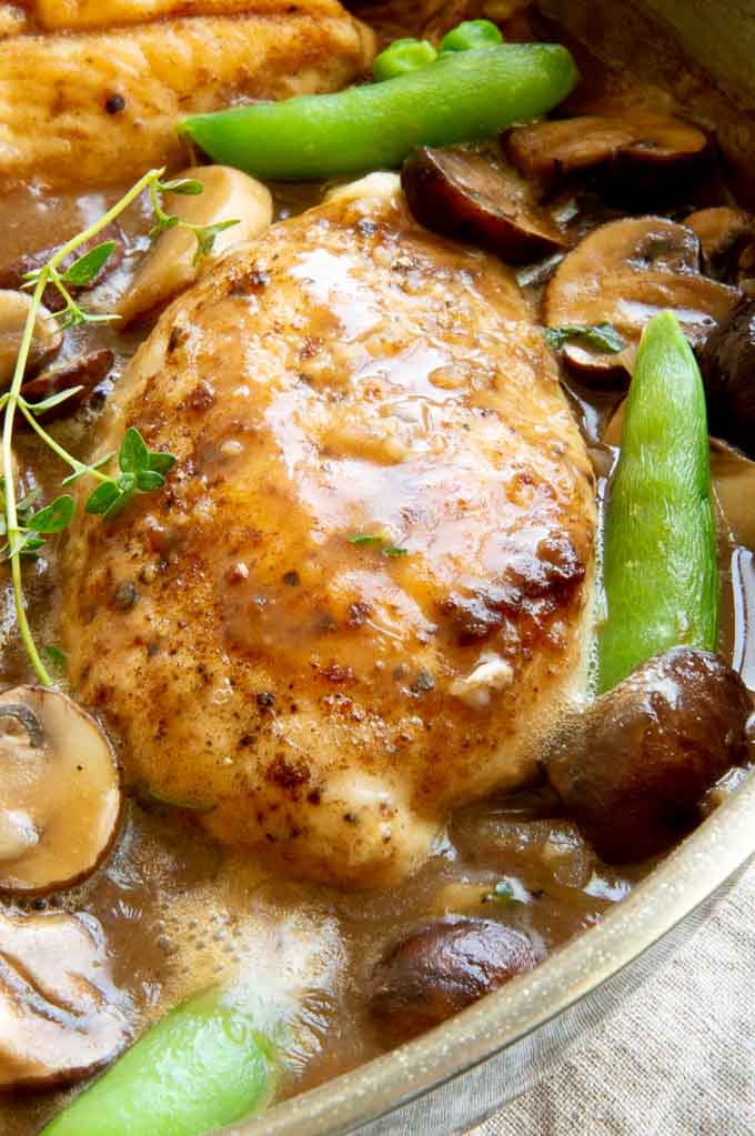 Large chicken breast with lots of marsala sauce and mushrooms on top in a pan