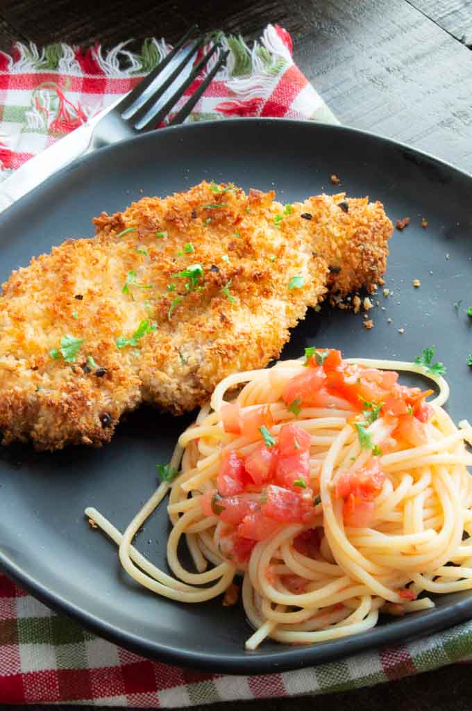 Pasta and pork schnitzel on a black plate