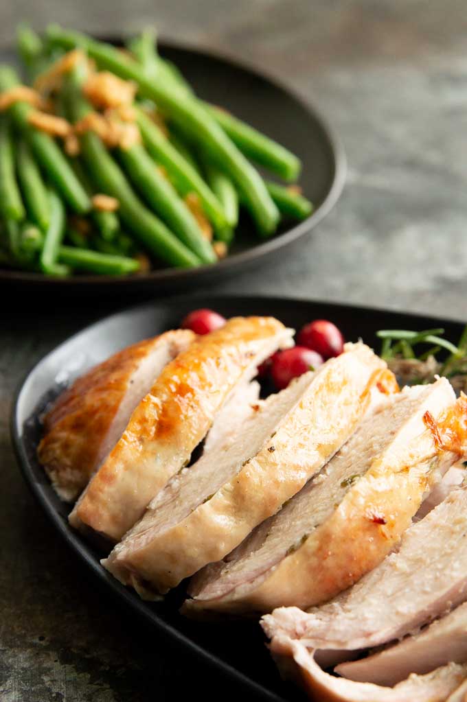 Sliced juicy turkey on a black plate with cranberries and green beans