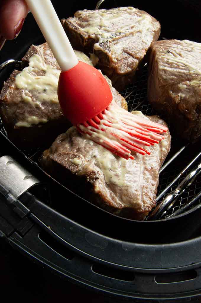 partially cooked lamb chops being brushed with a sauce to create a glaze