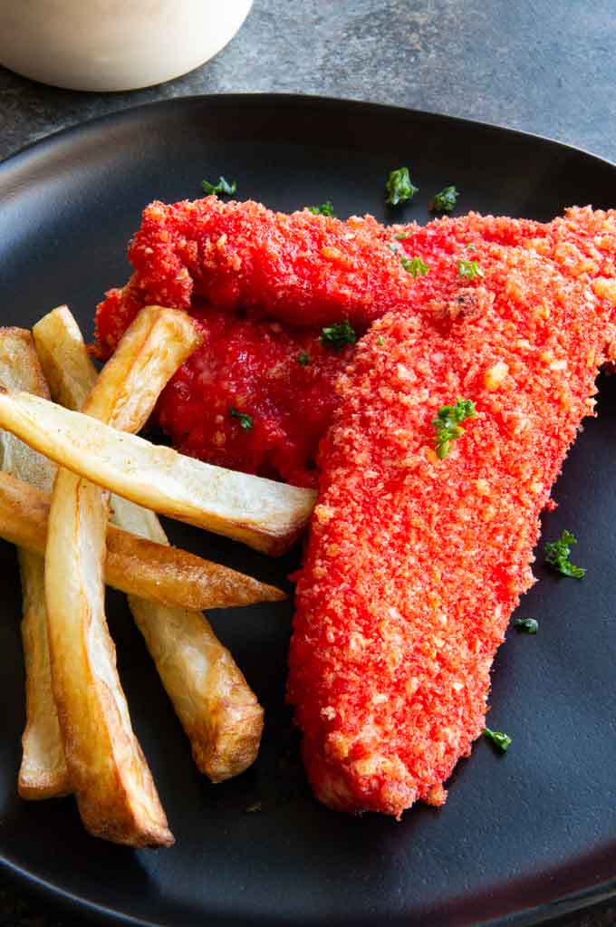 Cheeto coated chicken breast tenders next to french fries on a black plate