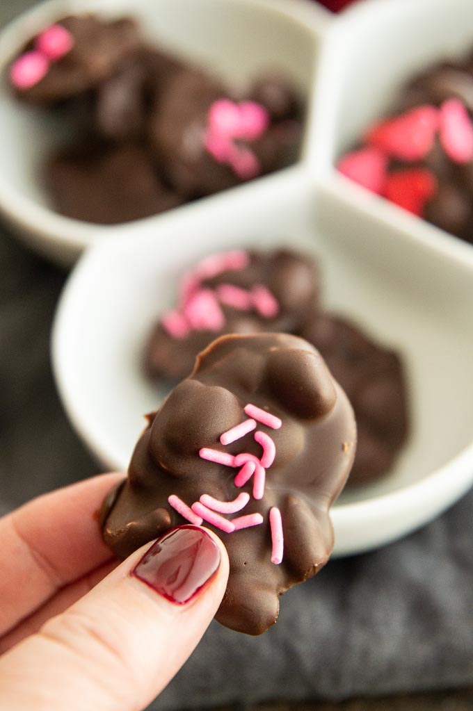 Picking up a peanut cluster with pink sprinkles on them from a candy bowl