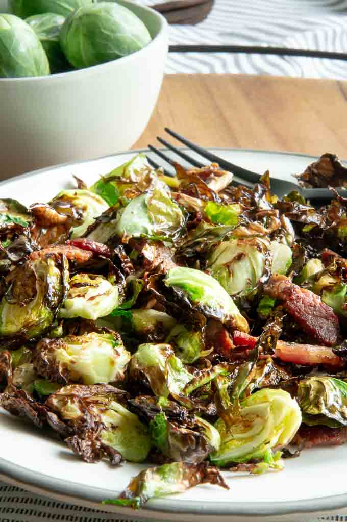 Serving plate (white) with fresh air fryed sprouts and bacon being served with a black fork