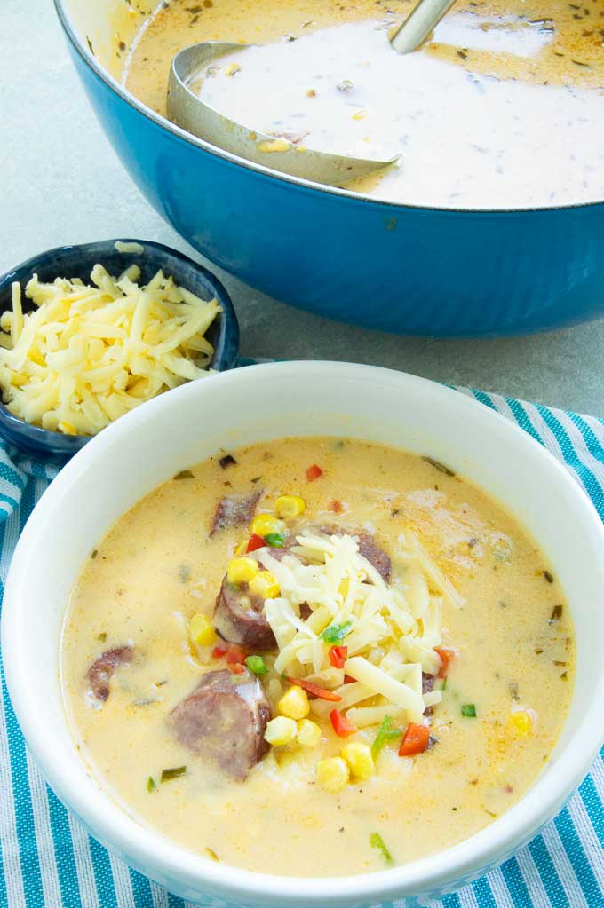 hearyt bowl of corn chowder topped with cheese and bratwurst on the table