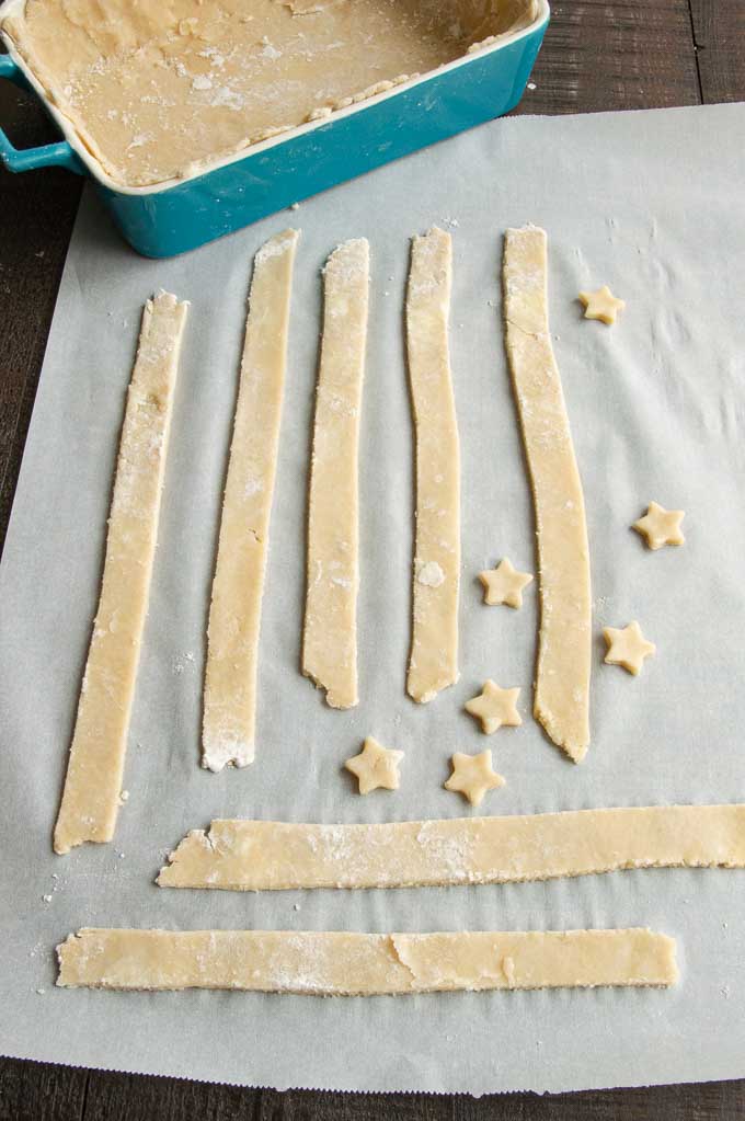 Cut pieces of stars and stripes out of pie dough on a table