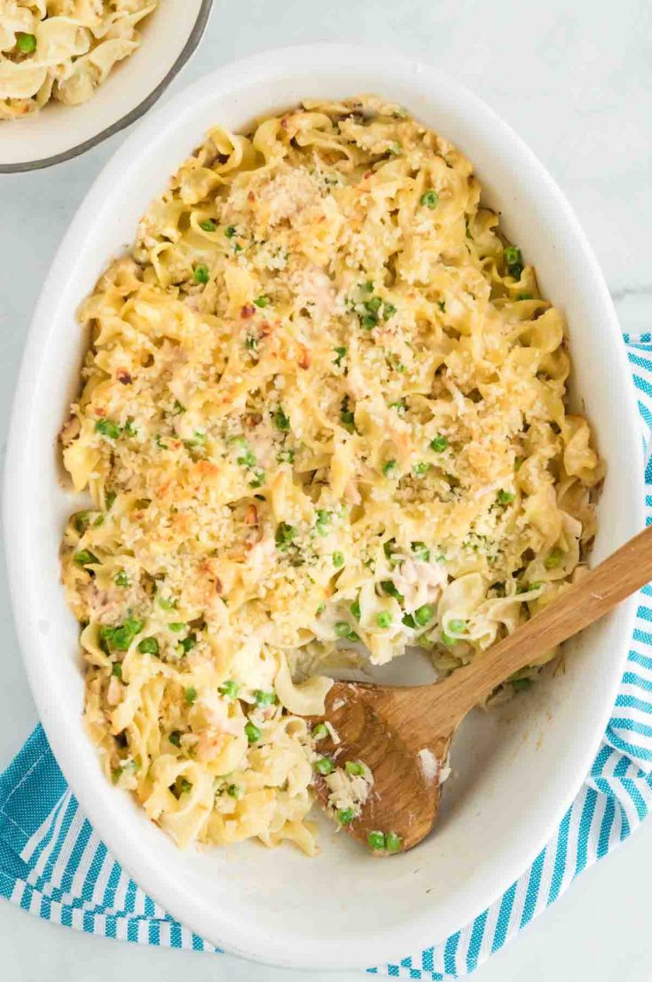 baking dish full of tuna and noodles with a wooden spoon scooping it out