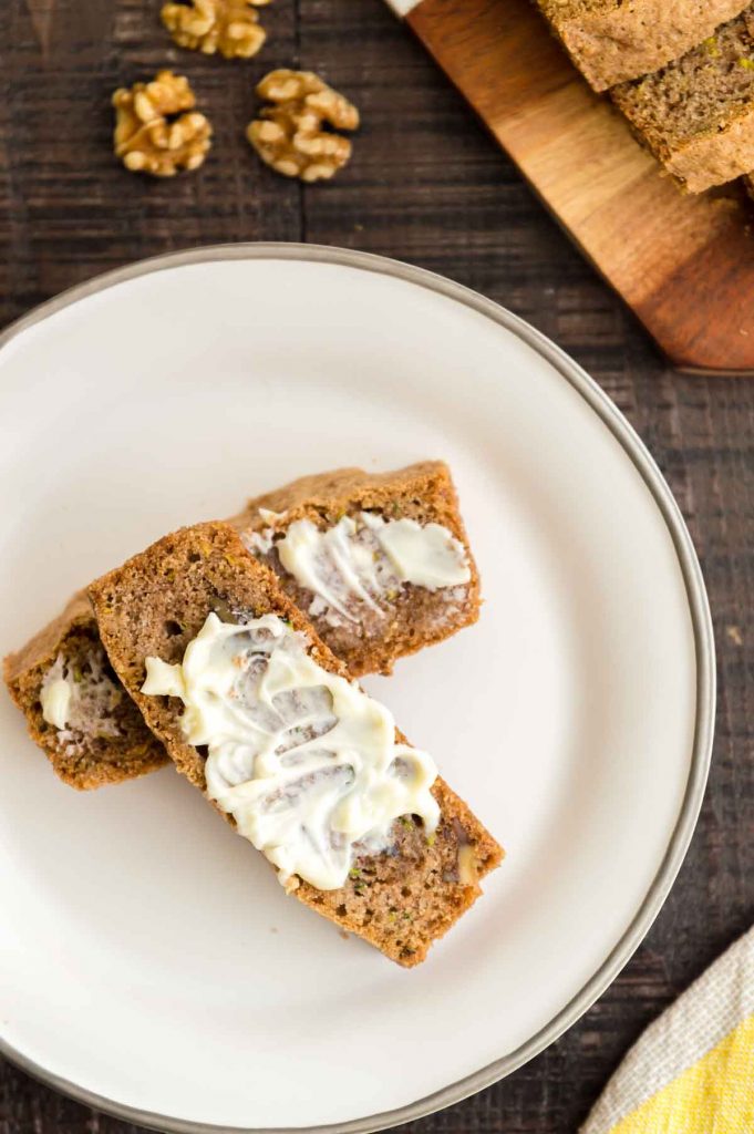 Zucchini bread with butter slathered over the top of it on a plate