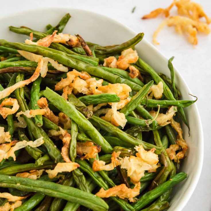 close up of green beans in a bowl with onions on top