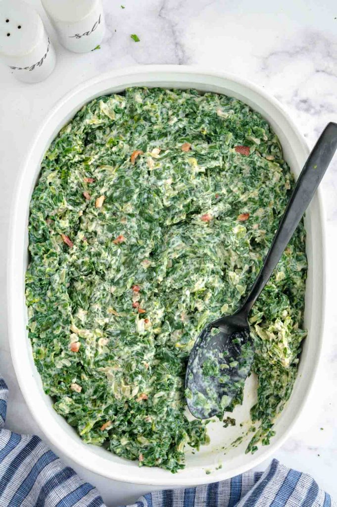 serving bowl of creamed spinach with black spoon being dipped