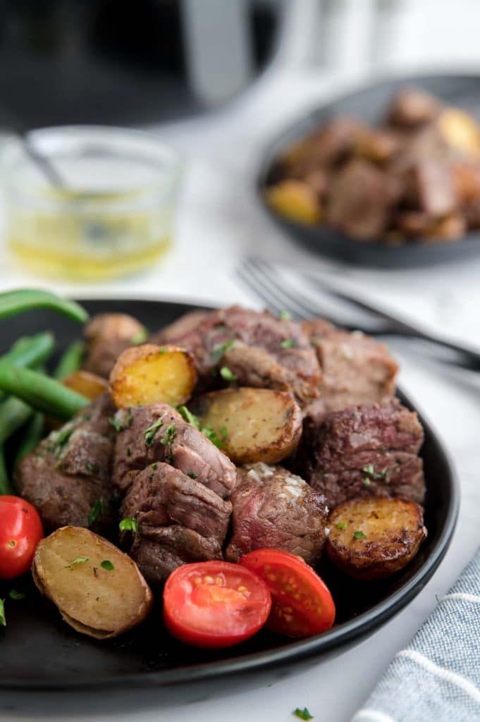 Steak bites and potatoes on a black plate with an air fryer in the background
